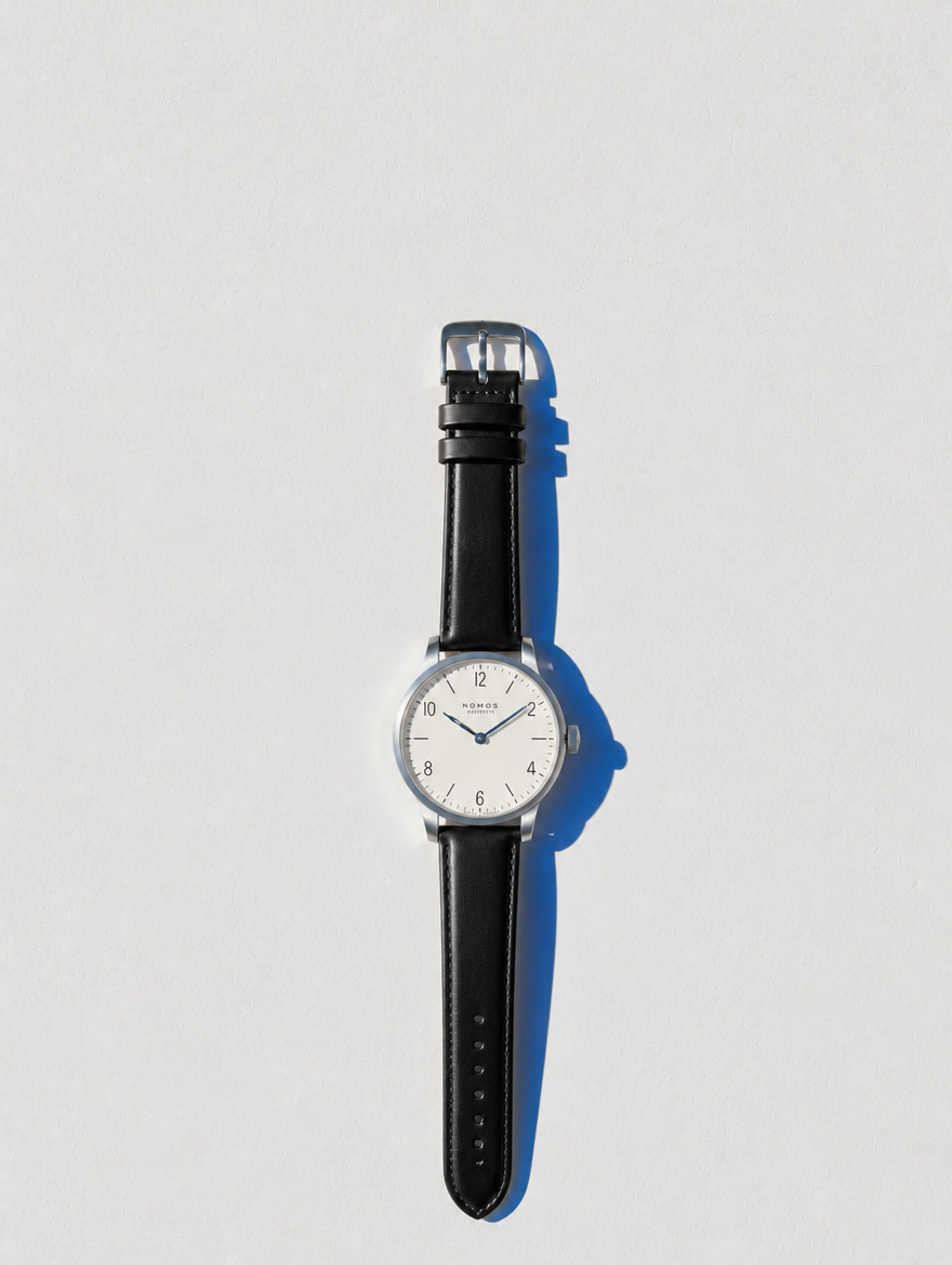 Nomos Tangente completo en flat lay sobre pared Santorini